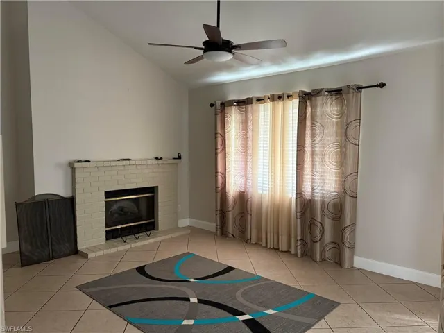 Unfurnished living room featuring a brick fireplace, a ceiling fan, vaulted ceiling, and light tile patterned floors