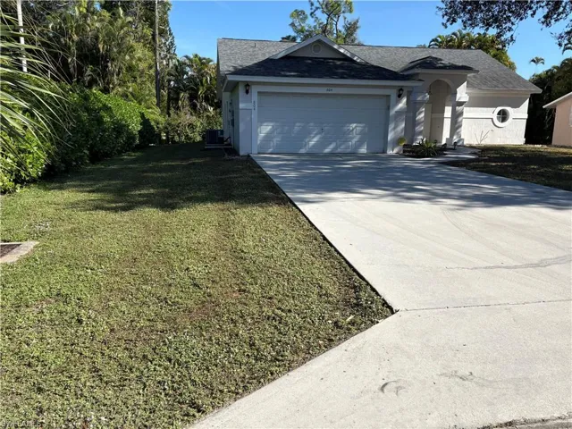 View of front of house with concrete driveway, a front lawn, a garage, and a shingled roof