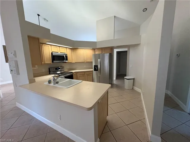 Kitchen featuring light countertops, light tile patterned floors, a high ceiling, appliances with stainless steel finishes, and a peninsula