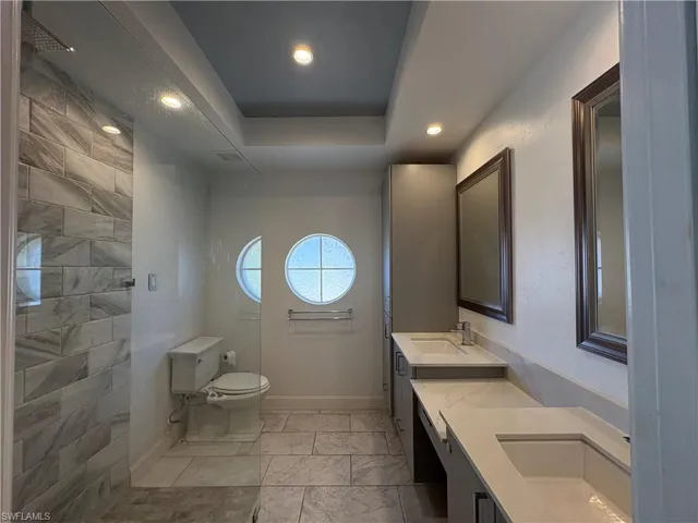 Bathroom with a tray ceiling, double vanity, recessed lighting, and a walk in shower