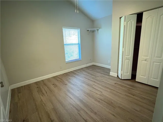 Unfurnished bedroom with wood finished floors, vaulted ceiling, and a closet