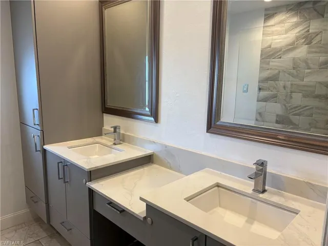Full bathroom with light marble finish flooring and two vanities