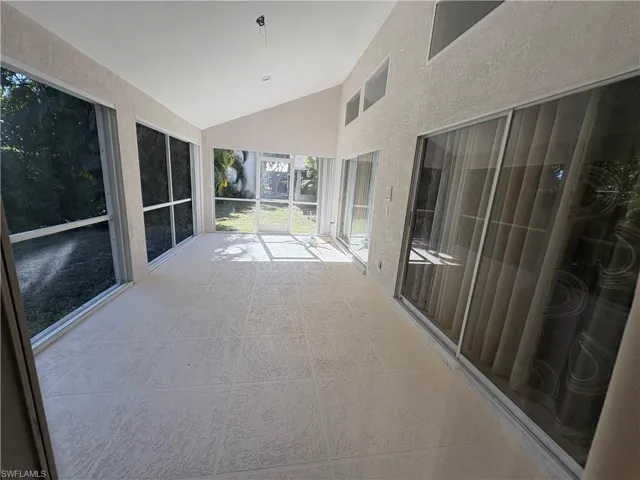 Unfurnished sunroom with a textured wall and high vaulted ceiling