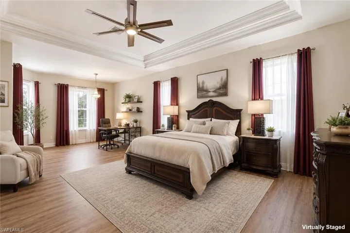Spacious interior featuring a multi-tiered tray ceiling with crown molding, wood-finish flooring, multiple windows, and a ceiling fan with integrated lighting