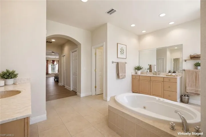 Spacious bathroom featuring a built-in soaking tub, dual vanity with wood cabinetry, large mirror, and recessed lighting