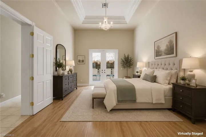 Spacious bedroom featuring wood-finish flooring, vaulted ceilings with crown molding, and a tray ceiling with a chandelier