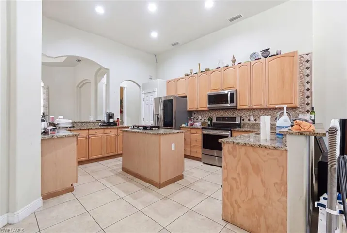 Kitchen featuring granite countertops, wood cabinetry, stainless steel appliances, and tile flooring
