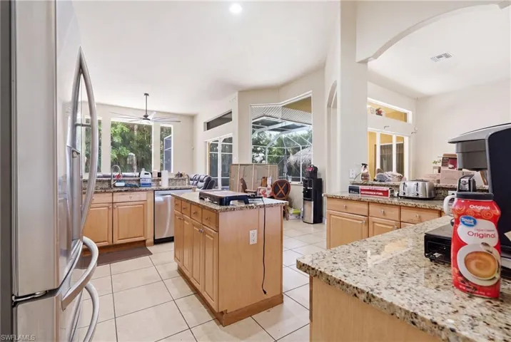 Open-concept kitchen featuring light wood cabinetry, stone countertops, stainless steel appliances, and a central island