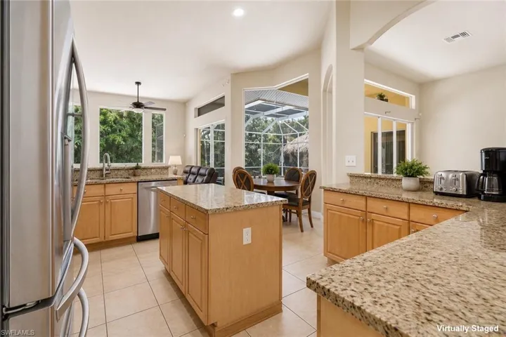 Kitchen featuring an island with ample cabinetry, light wood-finish cabinetry, speckled countertops, stainless steel appliances, and tiled flooring