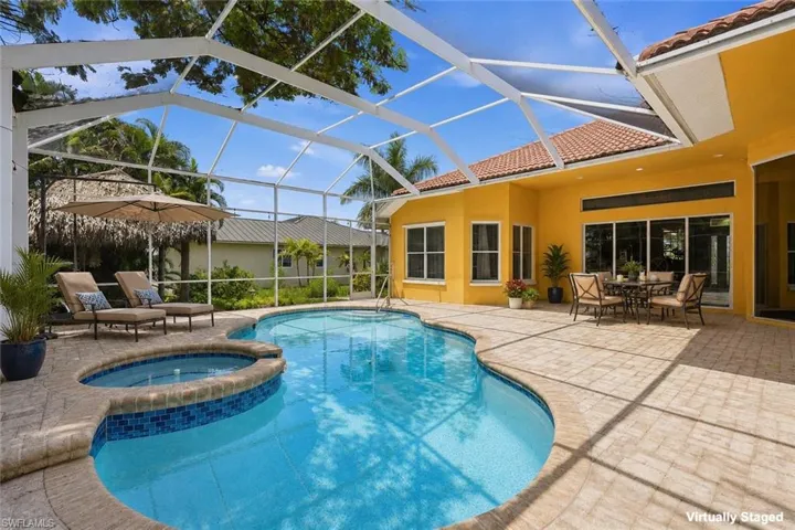 Screened lanai featuring a free-form swimming pool with an integrated spa, paver decking, and a stucco exterior with a tile roof