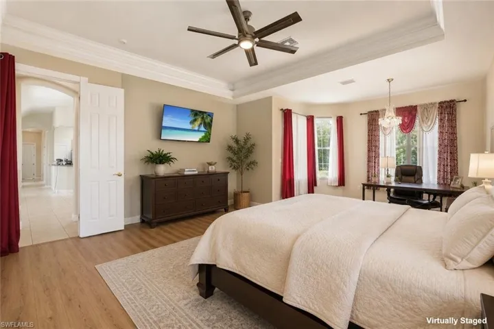 Spacious bedroom featuring wood-finish flooring, a tray ceiling with a ceiling fan, and multiple windows