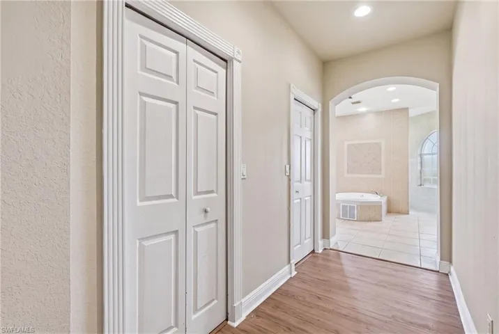 Hallway featuring wood-finish flooring, recessed lighting, and an arched doorway leading to a tiled room