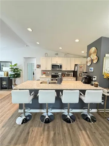 Kitchen featuring appliances with stainless steel finishes, vaulted ceiling, light wood-style flooring, a kitchen bar, and white cabinetry
