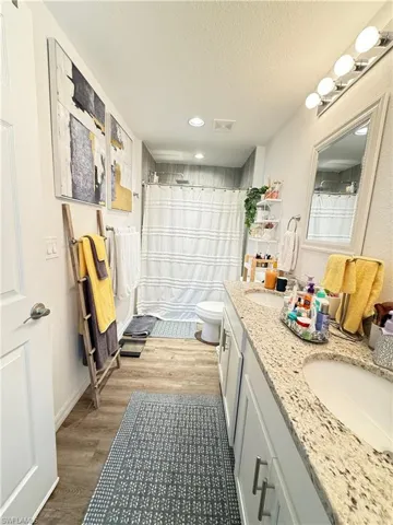 Bathroom with double vanity, wood finished floors, a textured ceiling, curtained shower, and recessed lighting