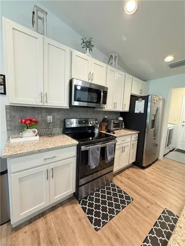 Kitchen featuring appliances with stainless steel finishes, lofted ceiling, backsplash, light wood-style flooring, and white cabinetry