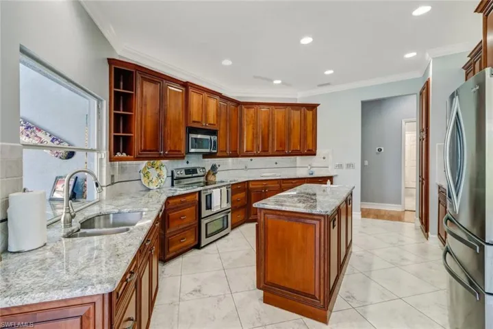 Kitchen with stainless steel appliances, light stone countertops, ornamental molding, open shelves, and a kitchen island