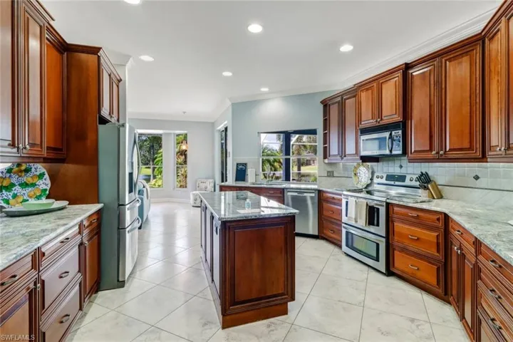 Kitchen featuring stainless steel appliances, light stone countertops, backsplash, ornamental molding, and a kitchen island