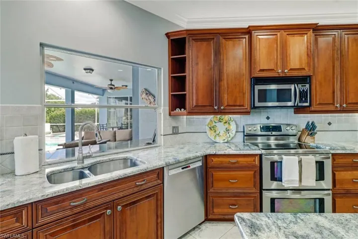 Kitchen with stainless steel appliances, light stone countertops, open shelves, backsplash, and wood finish cabinetry