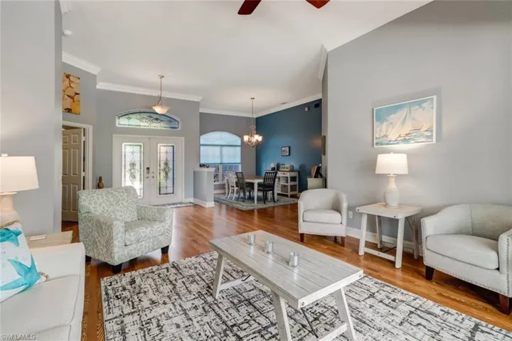 Living area featuring wood finished floors, ceiling fan, ornamental molding, a chandelier, and french doors