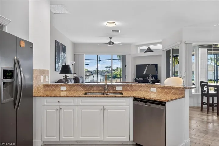 Kitchen with stainless steel appliances, white cabinetry, open floor plan, and dark stone counters