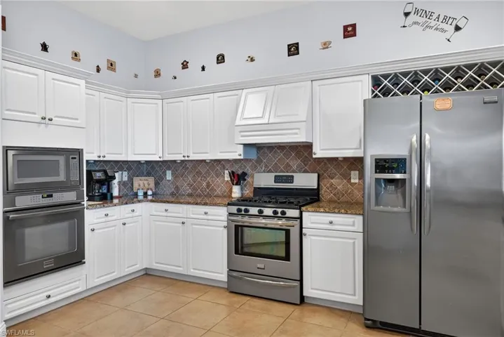Kitchen featuring appliances with stainless steel finishes, dark stone countertops, white cabinets, light tile patterned floors, and backsplash