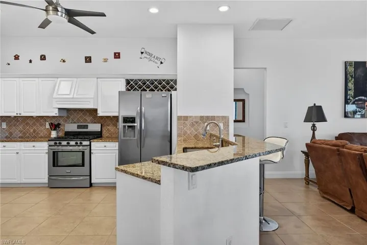 Kitchen featuring white cabinetry, stainless steel appliances, dark stone countertops, backsplash, and light tile patterned floors