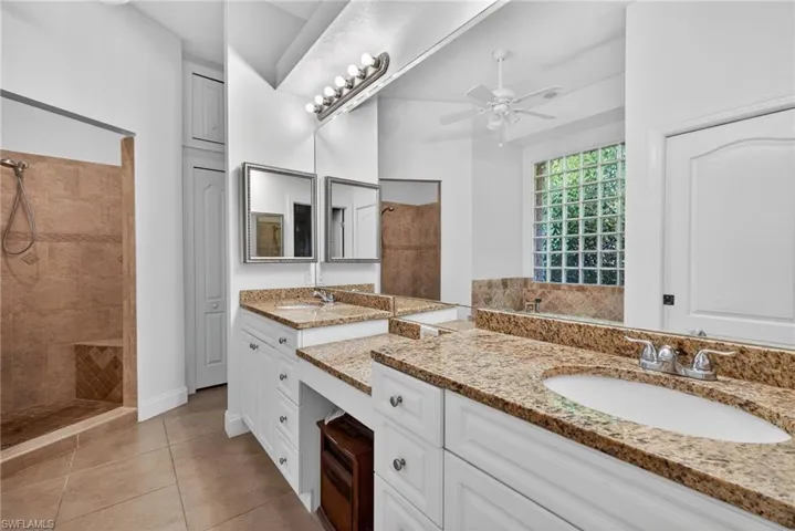 Full bathroom featuring vanity, tiled shower, light tile patterned floors, and ceiling fan