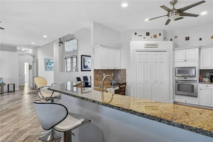 Kitchen featuring light stone counters, decorative backsplash, white cabinets, a ceiling fan, and recessed lighting