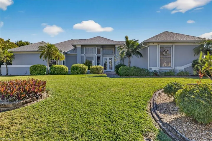 Ranch-style home with french doors, stucco siding, a front lawn, a shingled roof, and a balcony