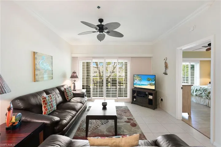 Living room with ceiling fan, crown molding, light tile patterned floors, and baseboards