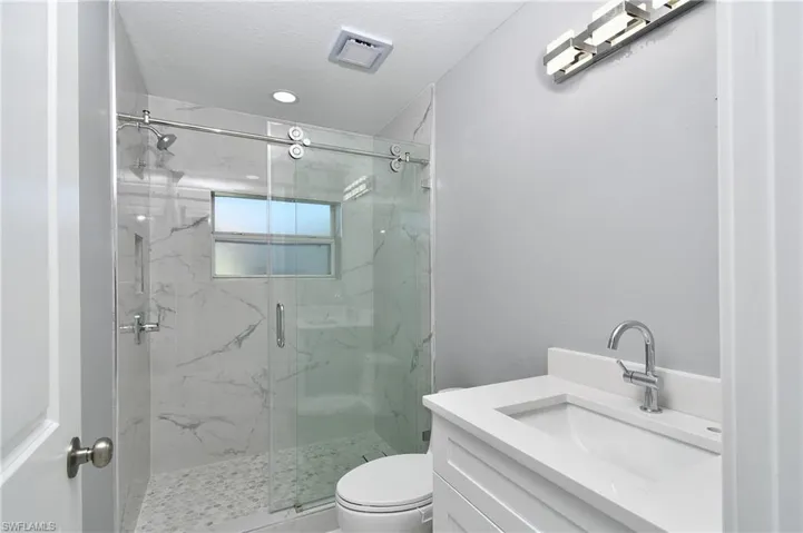 Full bathroom with toilet, vanity, a marble finish shower, and a textured ceiling