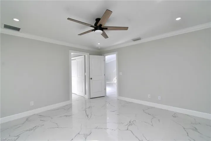 Empty room featuring a ceiling fan, crown molding, and visible vents