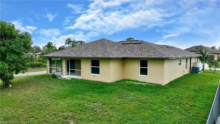 Back of house with stucco siding, a sunroom, central air condition unit, and a yard