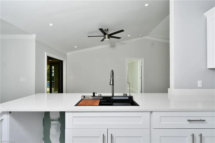 Kitchen with light countertops, ceiling fan, ornamental molding, white cabinetry, and a sink