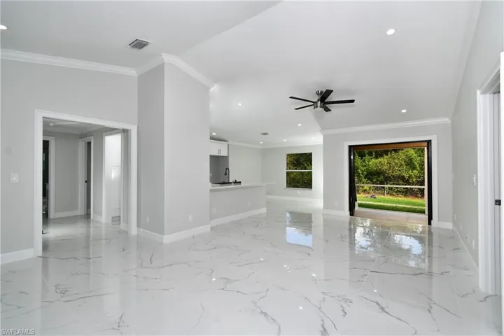 Unfurnished living room featuring a ceiling fan, crown molding, and baseboards