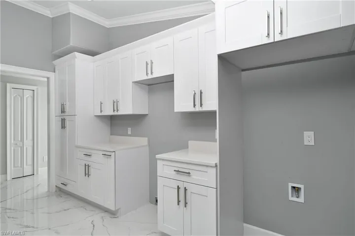 Kitchen featuring white cabinetry, marble finish floor, light countertops, and ornamental molding