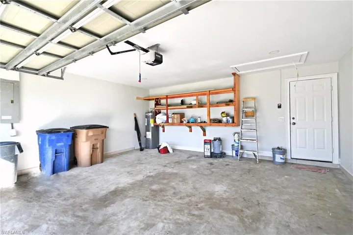 Garage featuring electric panel, a garage door opener, baseboards, and water heater