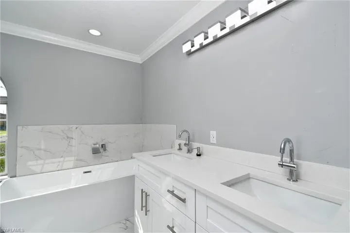 Bathroom with marble finish floor, a sink, a freestanding tub, and crown molding