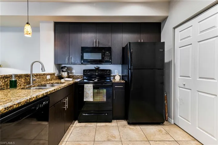 Kitchen featuring black appliances, light stone countertops, sink, light tile floors, and pendant lighting