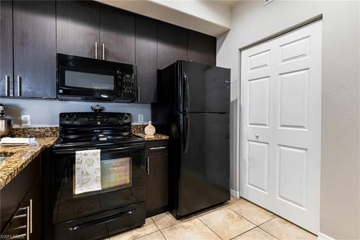 Kitchen featuring stone counters, black appliances, and light tile floors