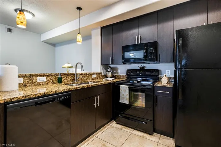 Kitchen featuring decorative light fixtures, light stone counters, black appliances, sink, and light tile floors