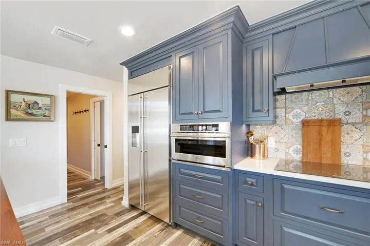 Kitchen with decorative backsplash, custom range hood, stainless steel appliances, light wood-style floors, and blue cabinetry