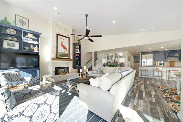 Living area with recessed lighting, a ceiling fan, stairway, dark wood-style flooring, and a stone fireplace