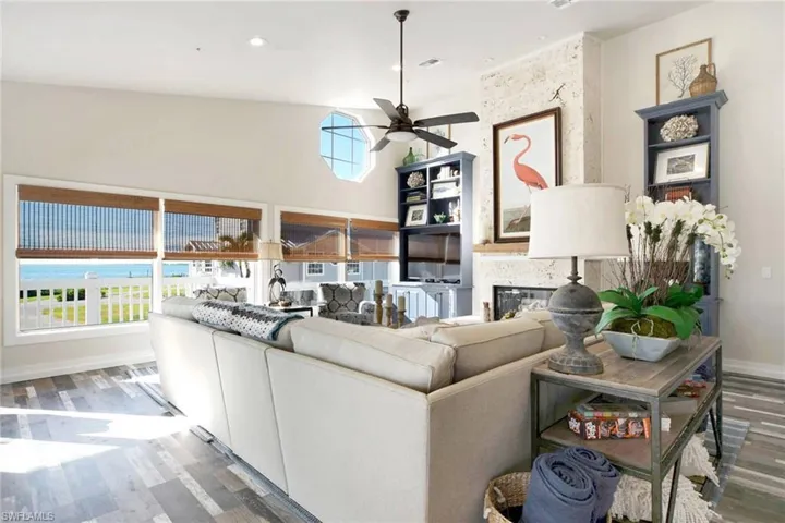Living area featuring wood finished floors, a glass covered fireplace, a ceiling fan, and a high ceiling