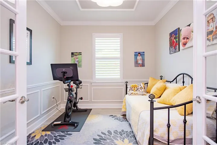 Room featuring French doors, decorative wainscoting, a tray ceiling with crown molding, and plantation shutters