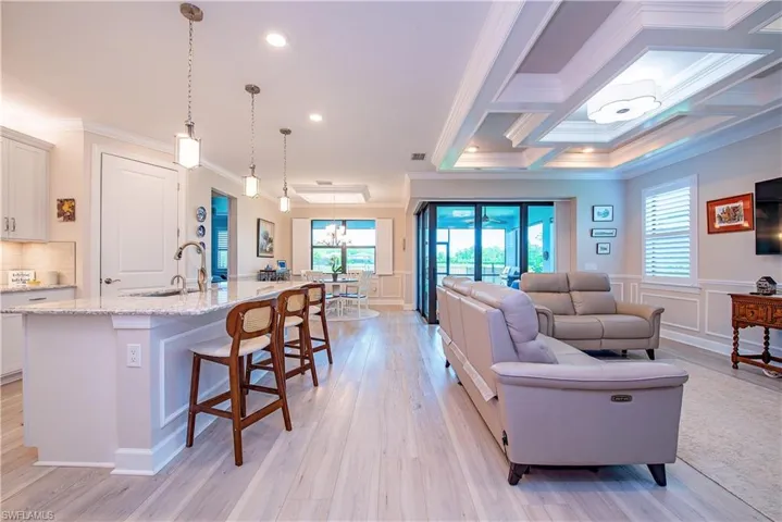Open-concept living area with light wood-finish flooring, a kitchen island featuring a granite countertop, pendant lighting, and recessed ceiling lighting