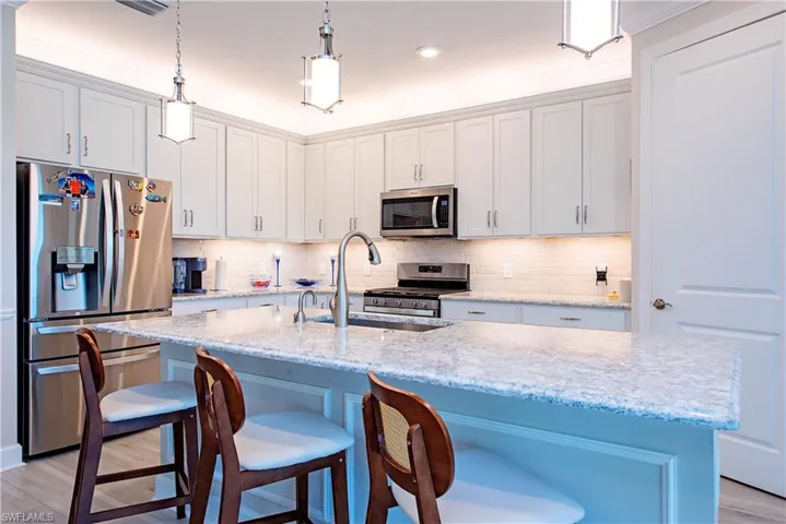 Kitchen featuring an expansive island with a light-toned countertop, white cabinetry with crown molding, stainless steel appliances, pendant lighting, and a subway tile backsplash