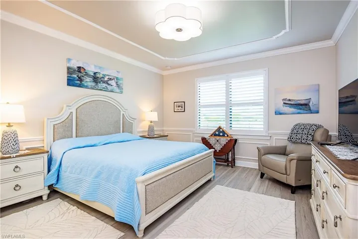 Spacious room featuring tray ceiling with crown molding, decorative chair rail, wide window with plantation shutters, and wood-finish flooring