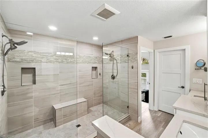 Expansive walk-in shower with glass enclosures, dual shower heads, integrated wall niches, and a built-in bench