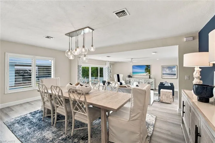 Open-concept living area featuring wood-finish flooring, a contemporary chandelier, white plantation shutters, and sliding glass doors